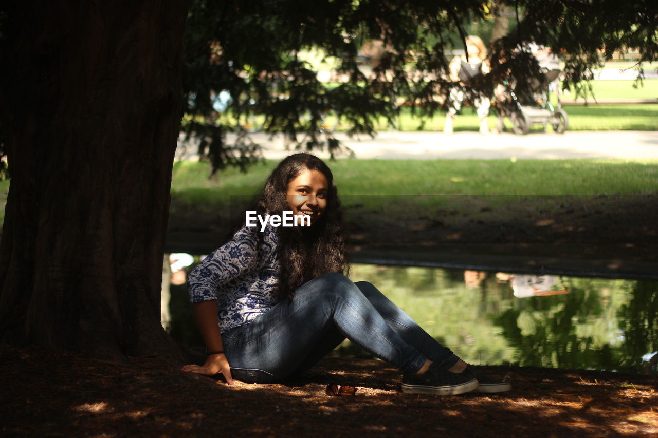 Portrait of young woman sitting by pond in forest