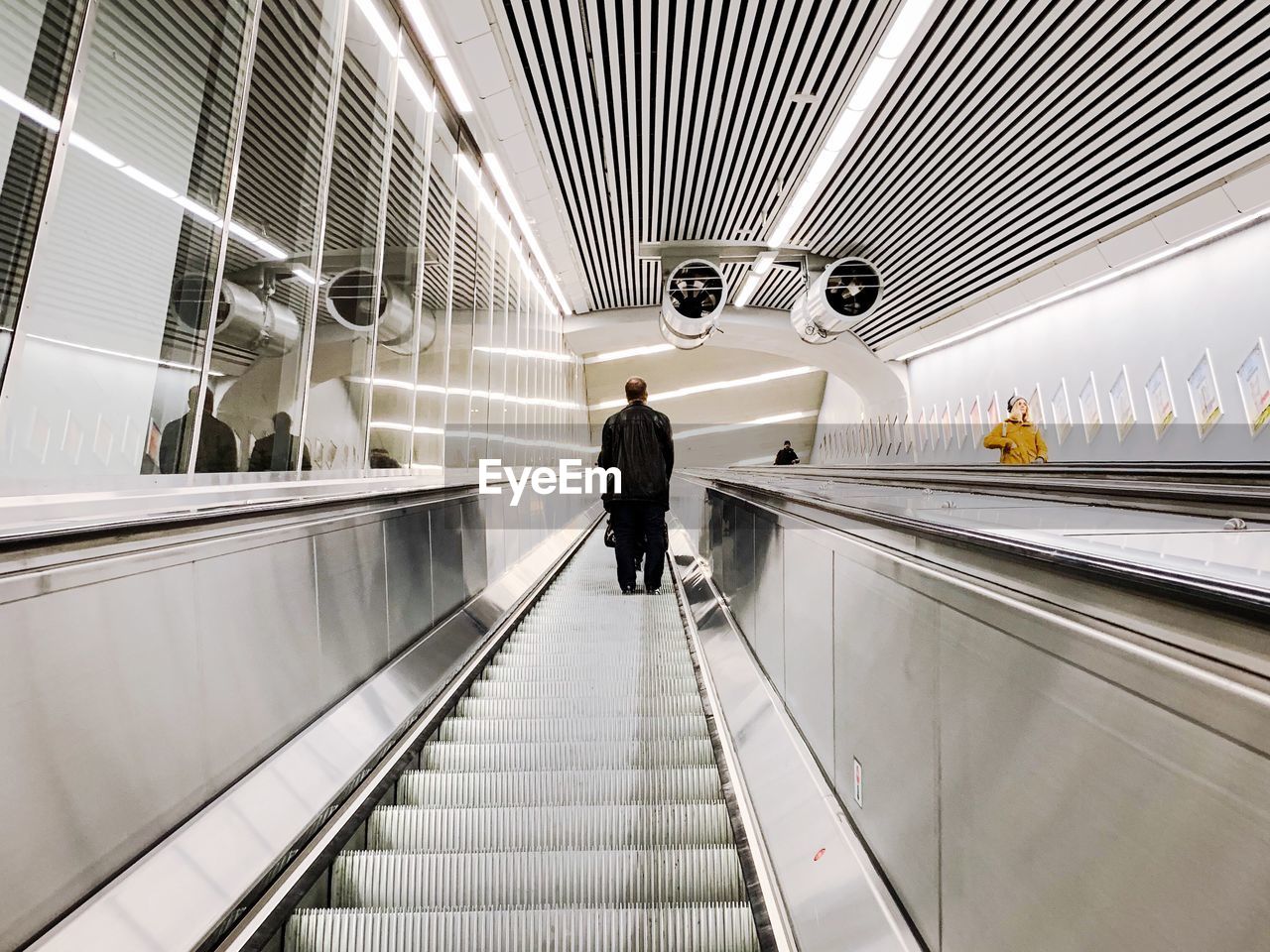 REAR VIEW OF MAN ON ESCALATOR AT AIRPORT