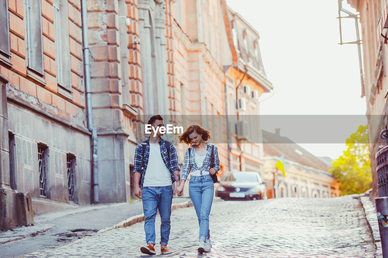 FULL LENGTH OF YOUNG COUPLE WALKING ON COBBLESTONE STREET