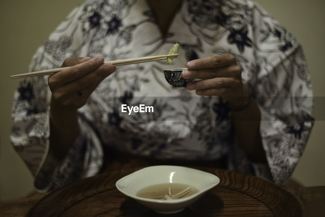 Close up view of hands of female caucasian woman in kimono using chopsticks to eat japanese food at ryokan