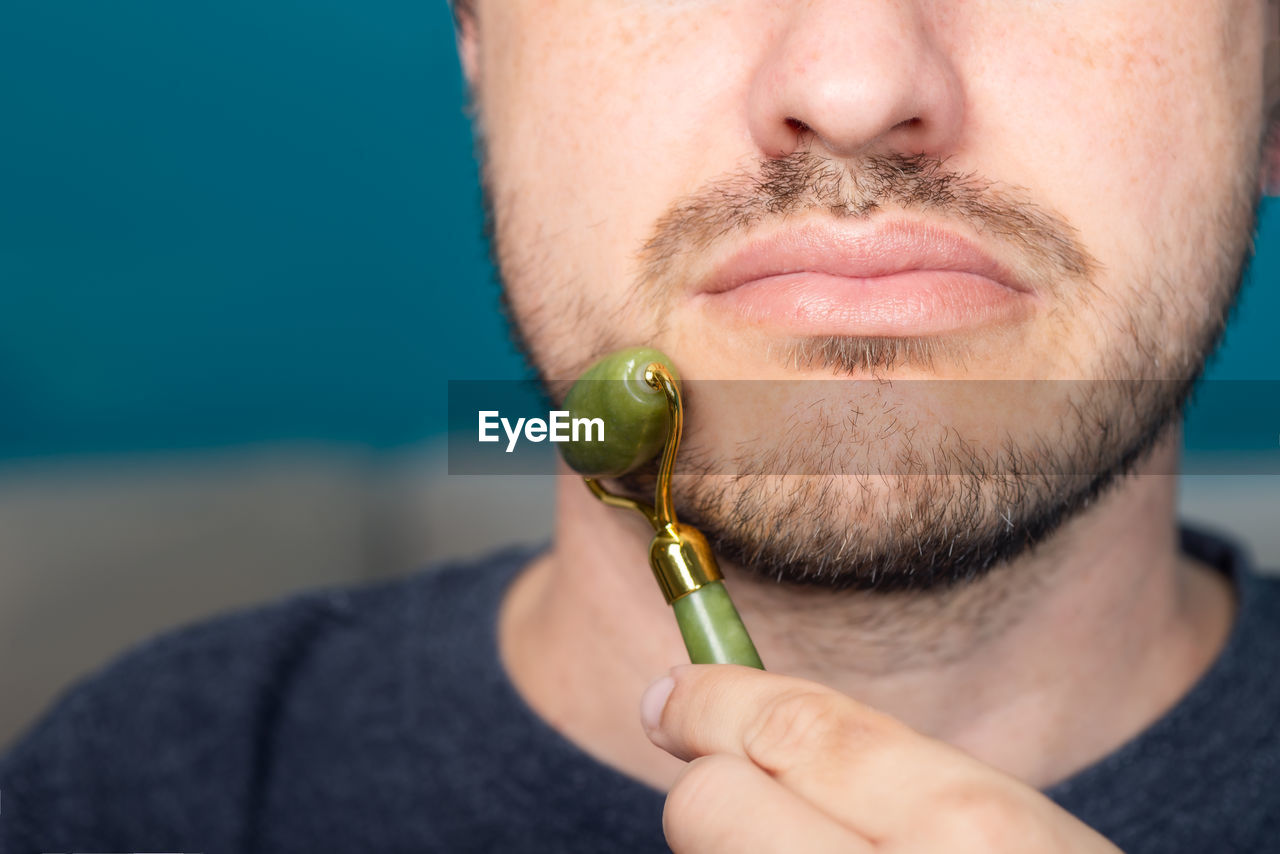 Bearded man is using jade face roller for beauty facial massage therapy