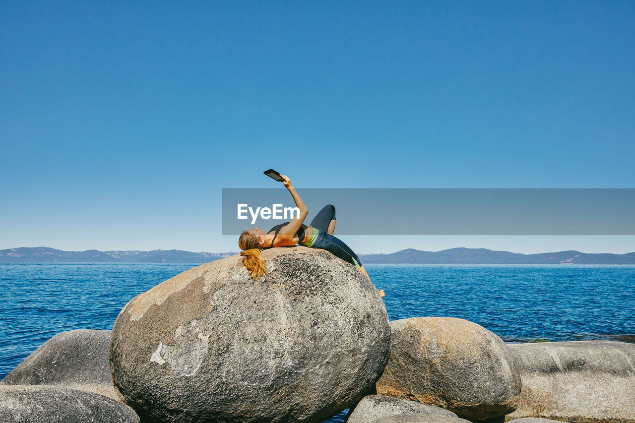 Young woman laying by lake tahoe reading a kindle book during the day
