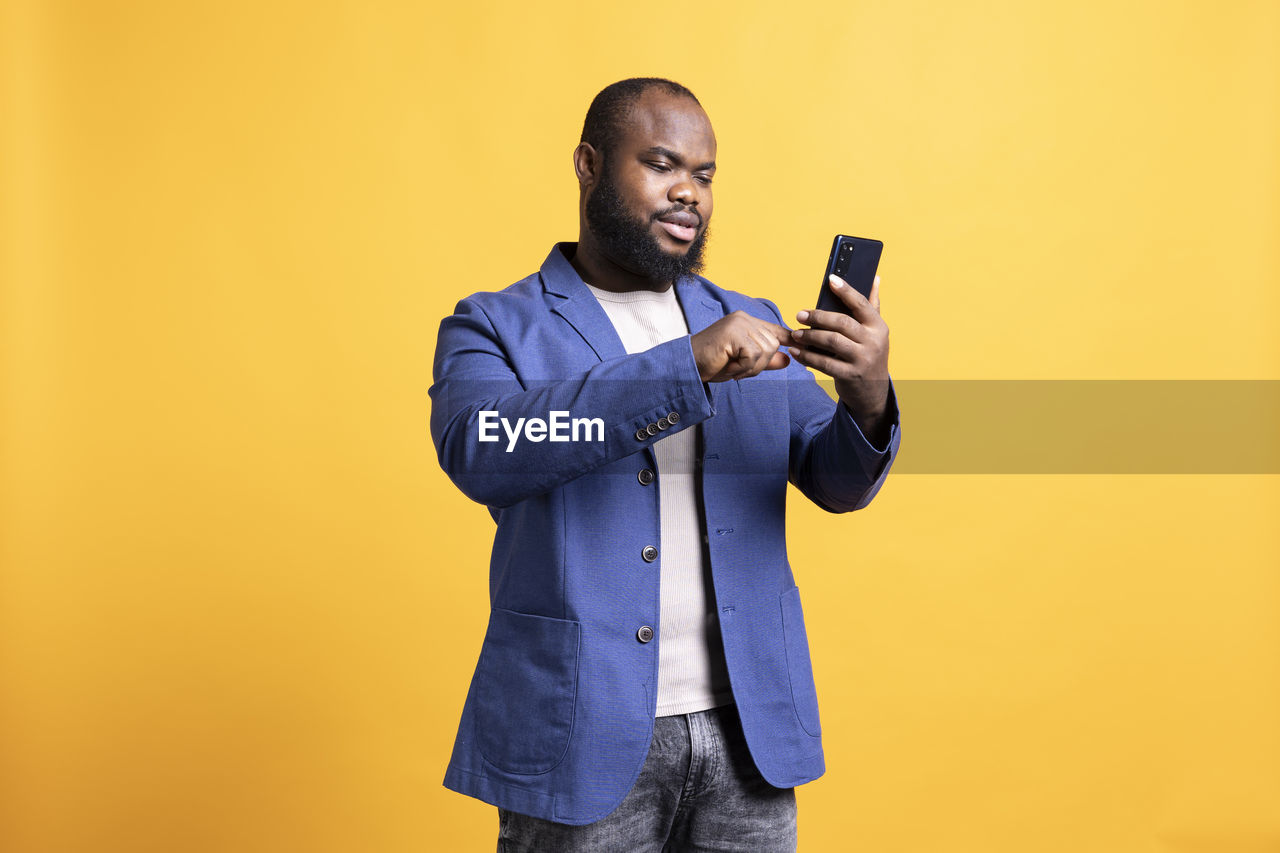 young man using mobile phone while standing against blue background