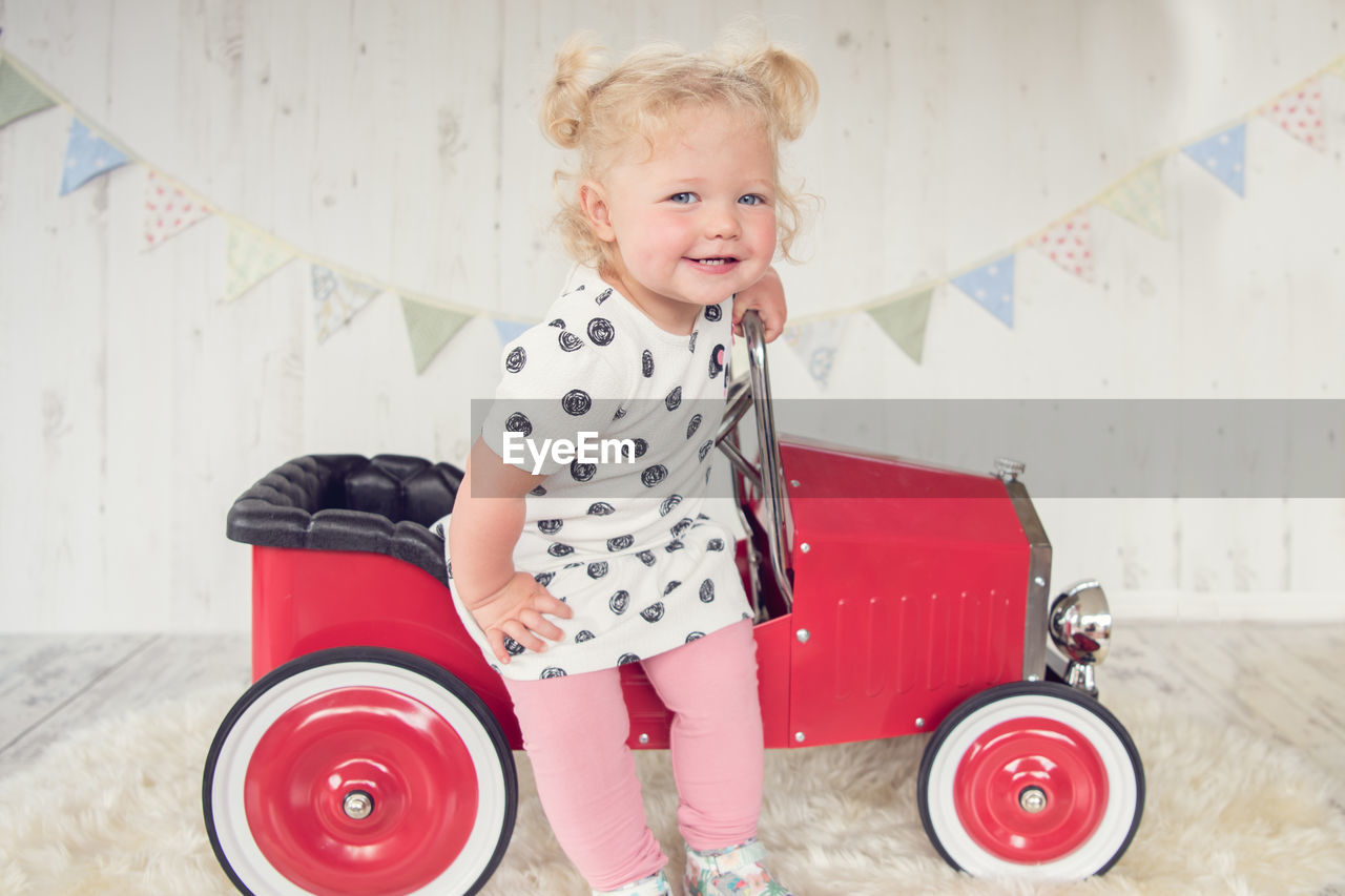 Portrait of cute baby girl standing by toy car