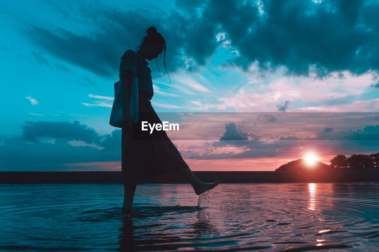 SILHOUETTE PERSON STANDING ON SEA AGAINST SKY DURING SUNSET