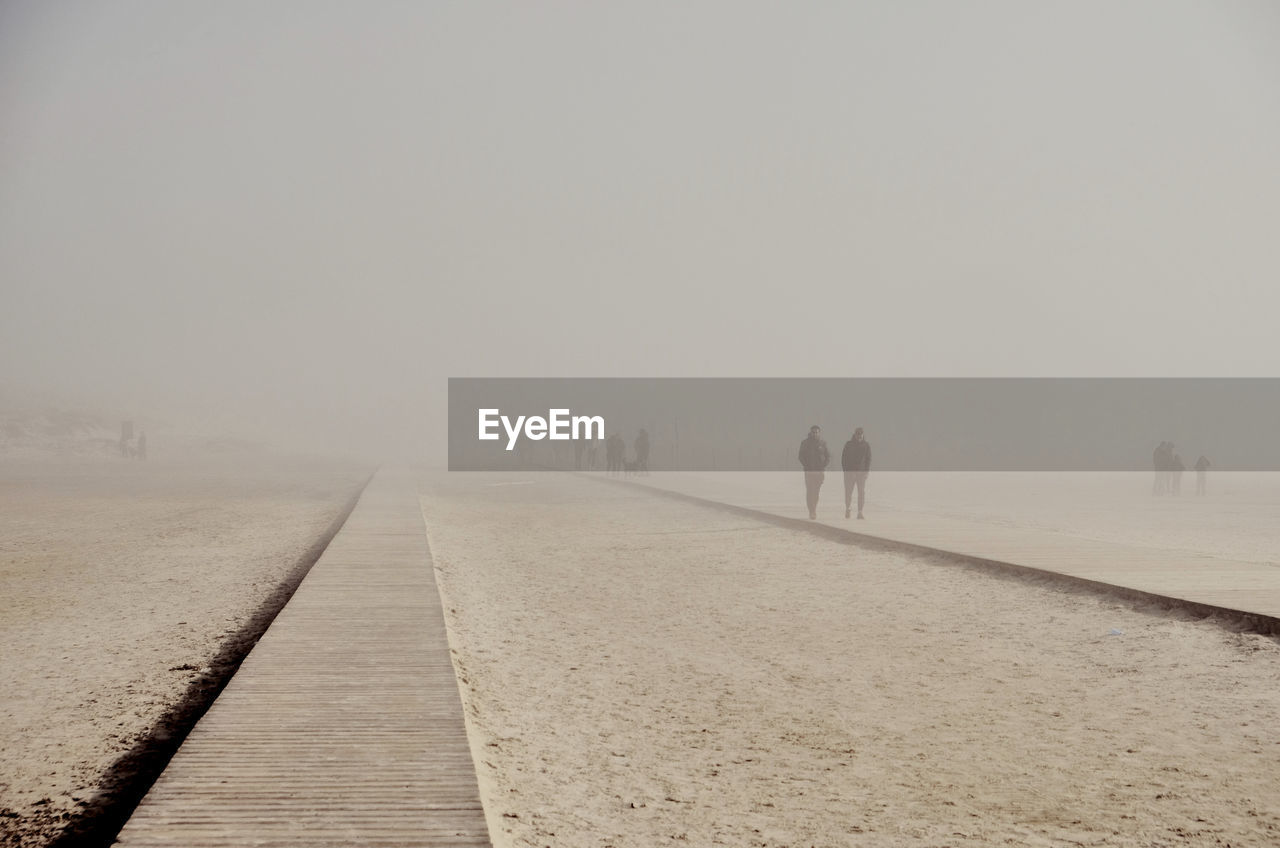 REAR VIEW OF PEOPLE WALKING ON ROAD