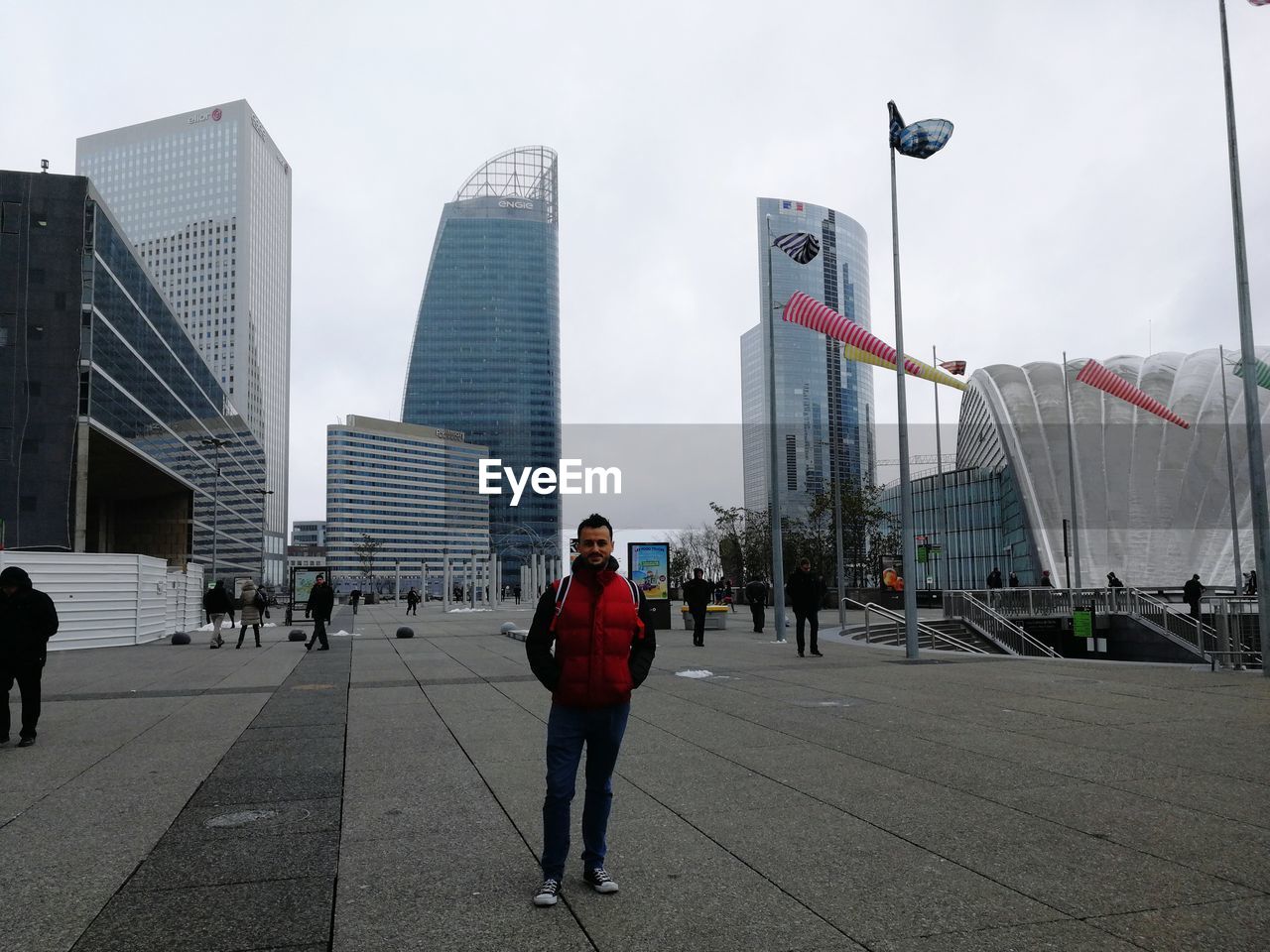 Portrait of mid adult man standing on street against sky in city