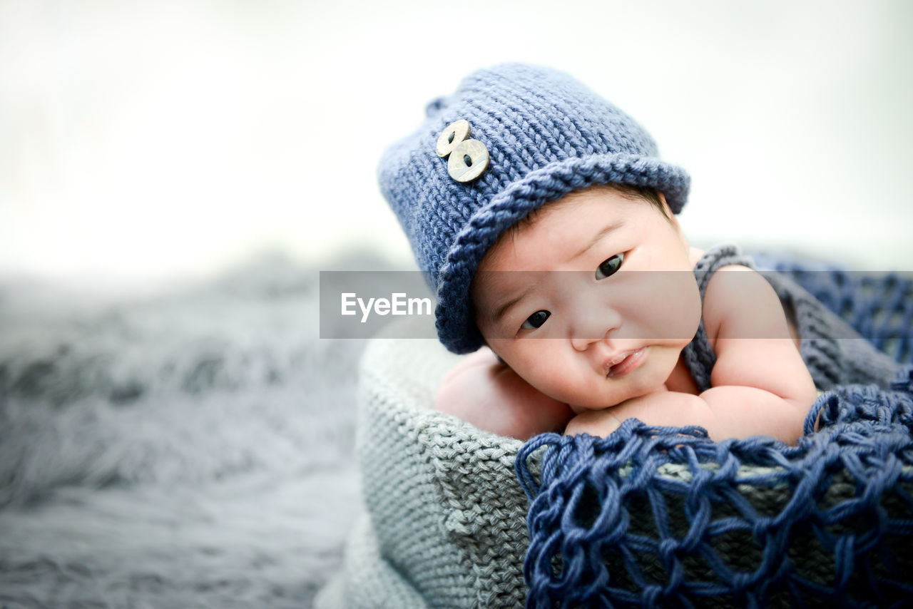 Close-up of cute baby boy lying down in basket on rug