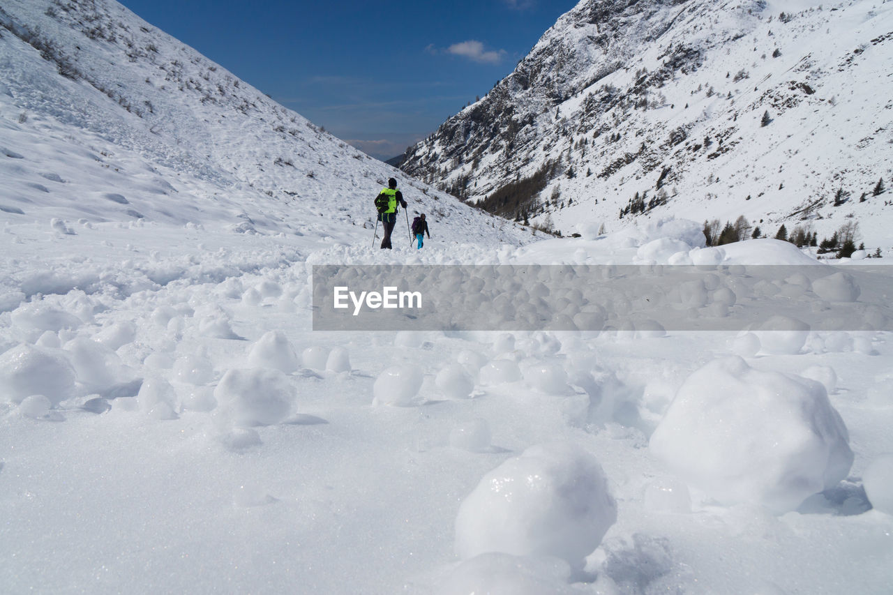 People walking on snowy landscape against sky