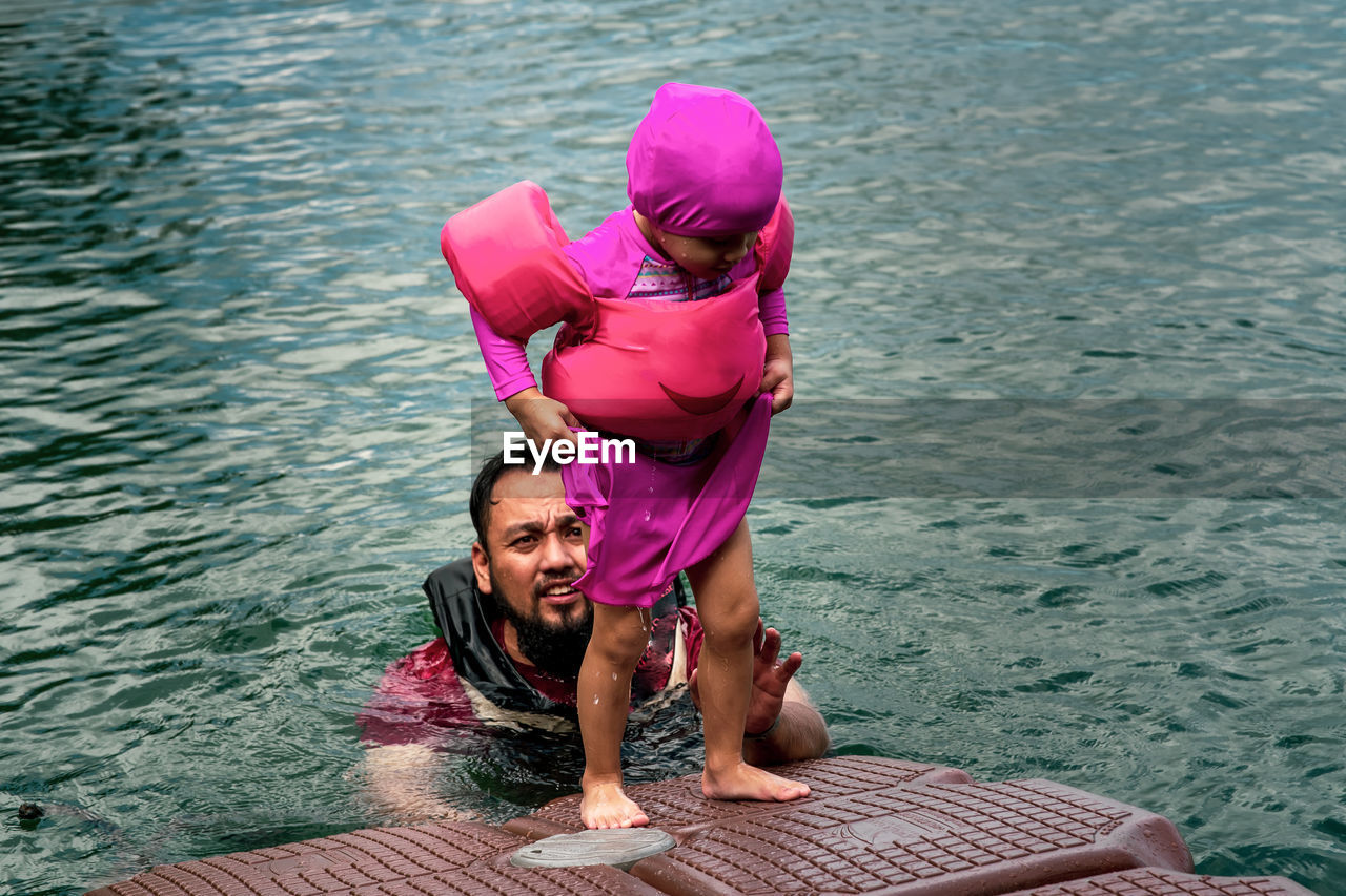 Full length portrait of happy girl in pink swimming suit with father in water.