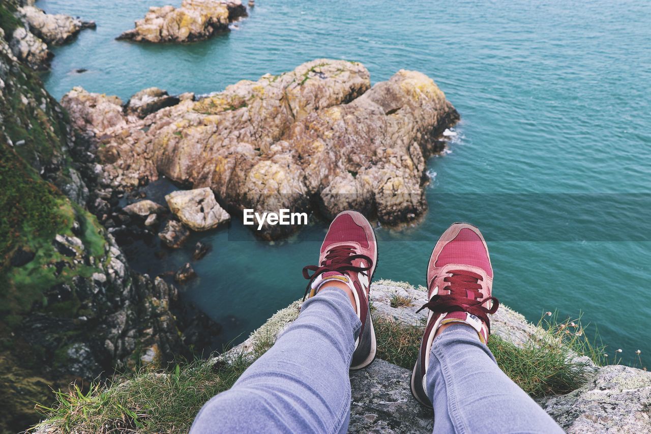 Low section of woman sitting on rock by sea