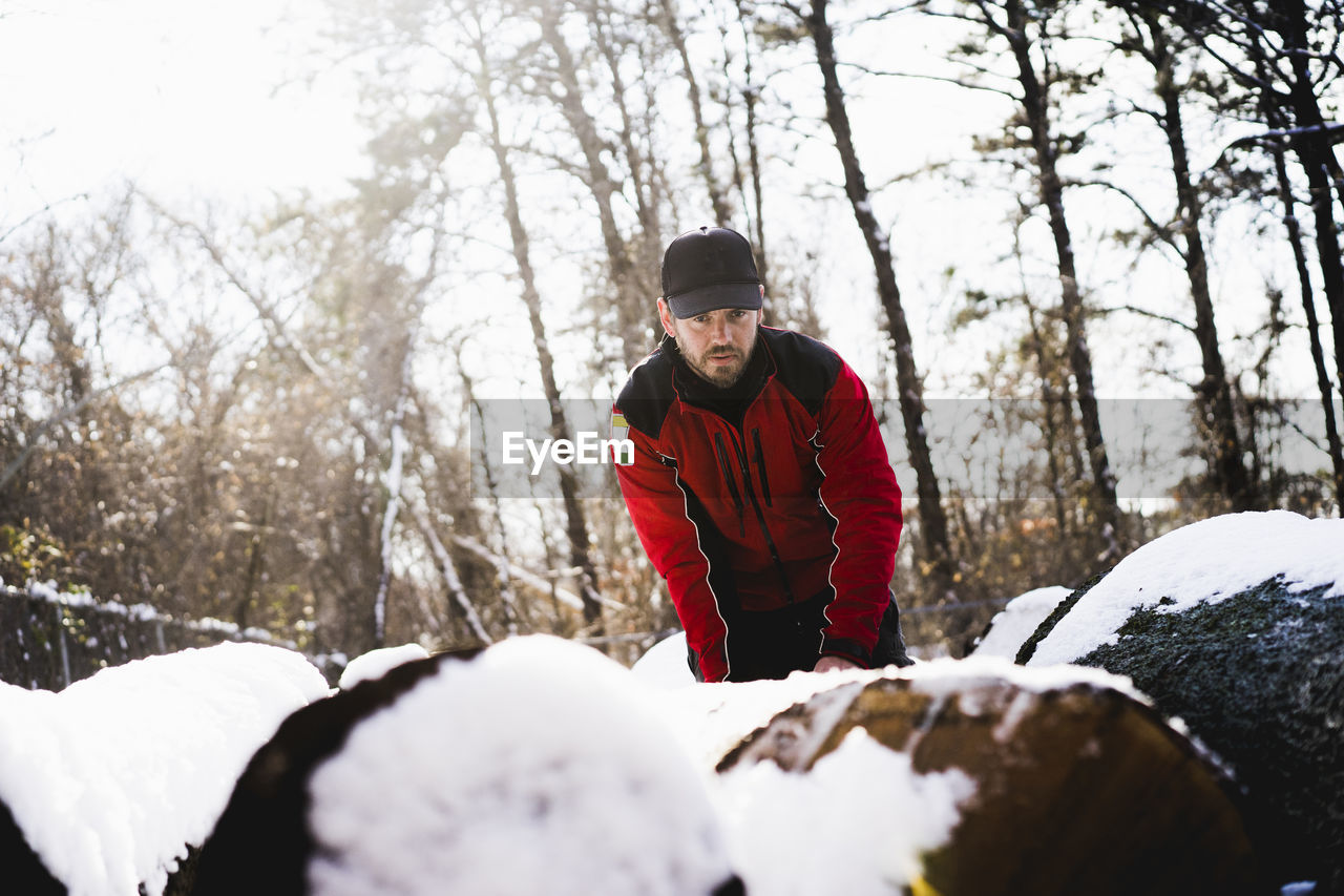 Low angle view of worker standing by snow covered fallen trees in backyard