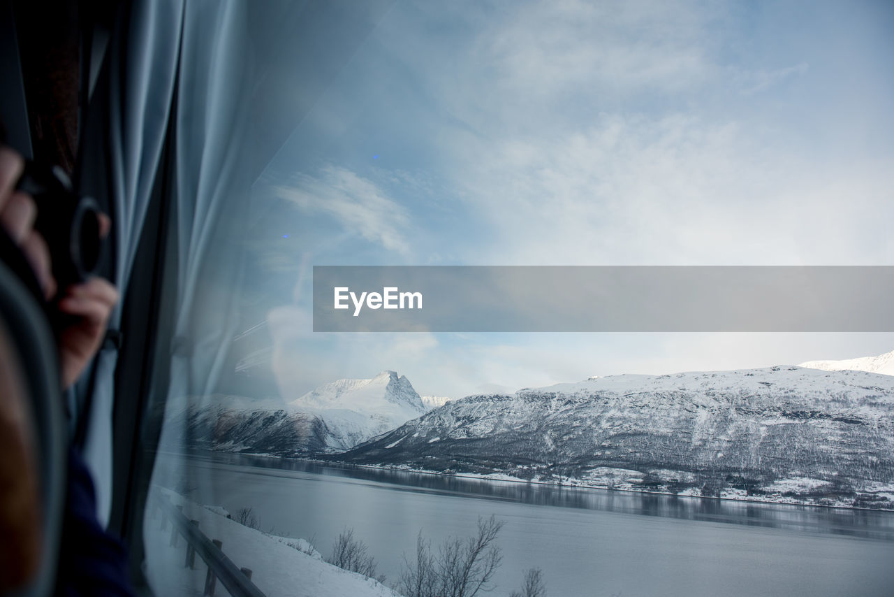 Close-up of hand photographing mountain through window during winter