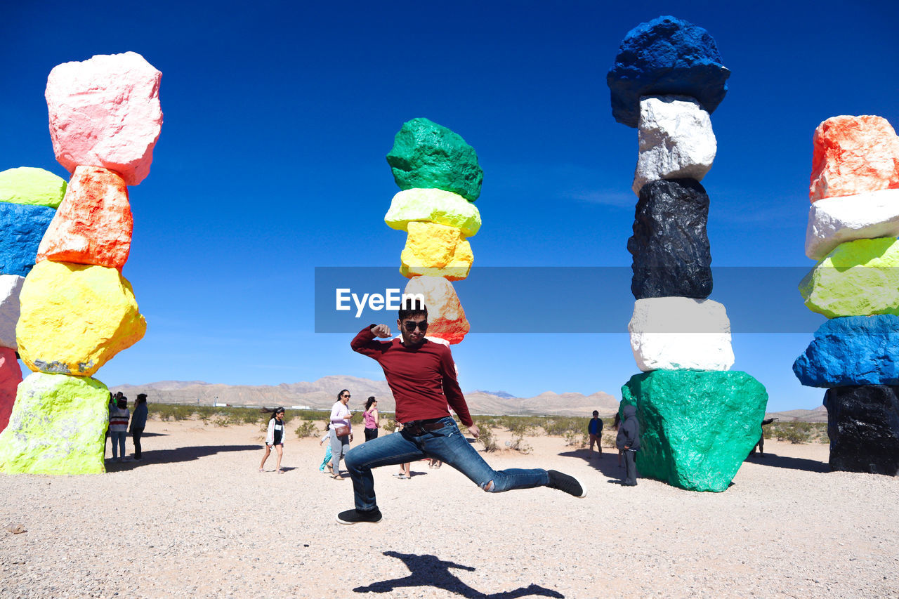Full length of man jumping against colorful stacked rocks in desert during sunny day