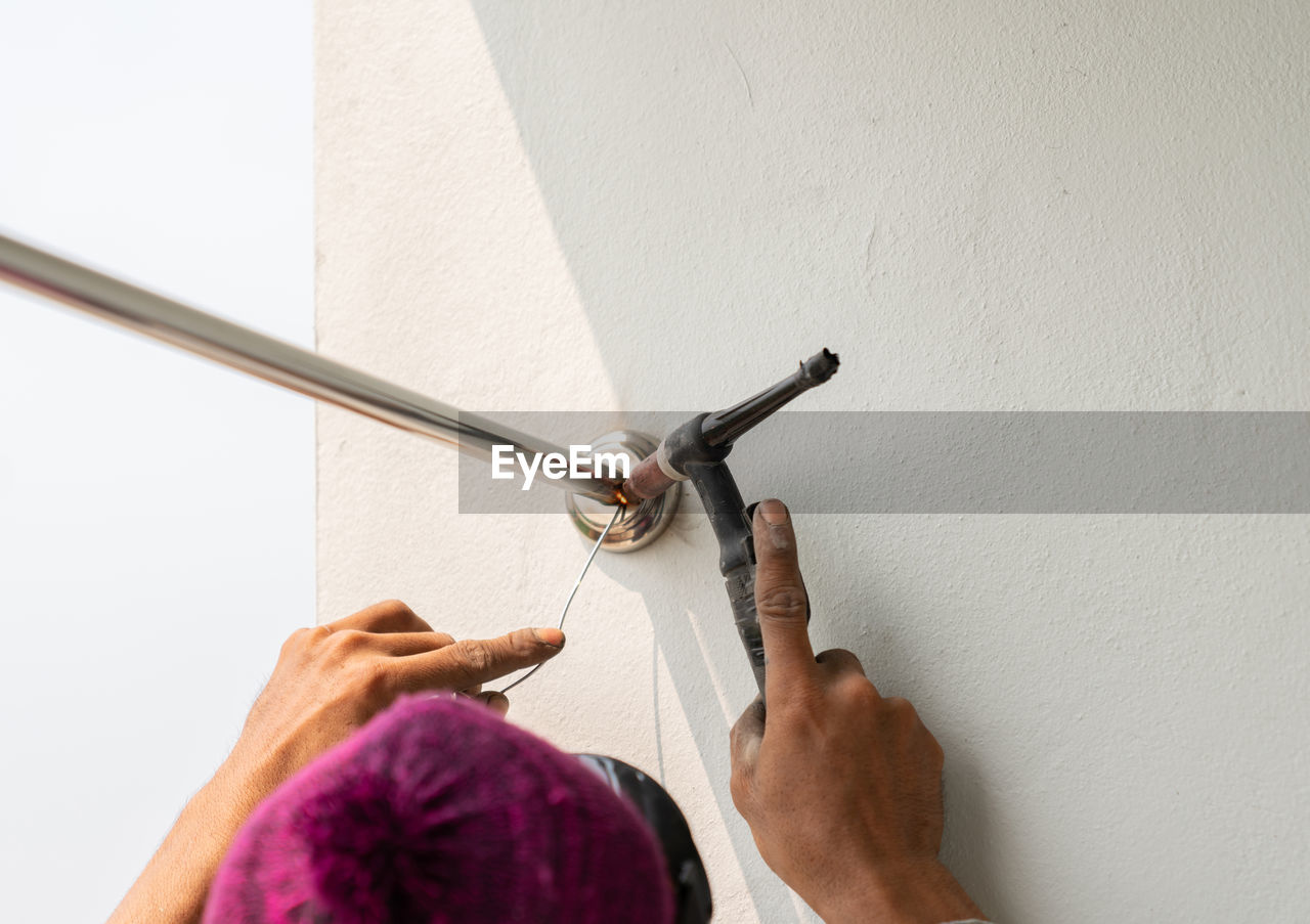 Worker welding stainless steel pipe clothesline in building.