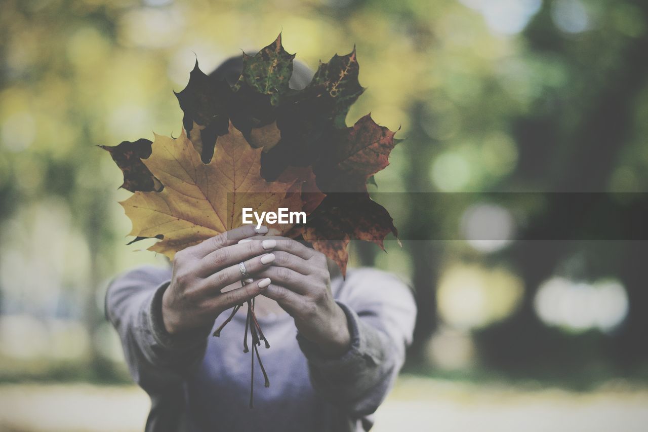 Woman covering face with leaves at park during autumn