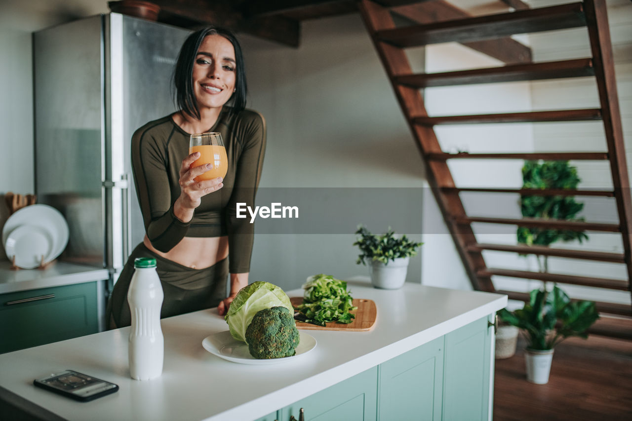 Smiling woman drinking juice in kitchen at home