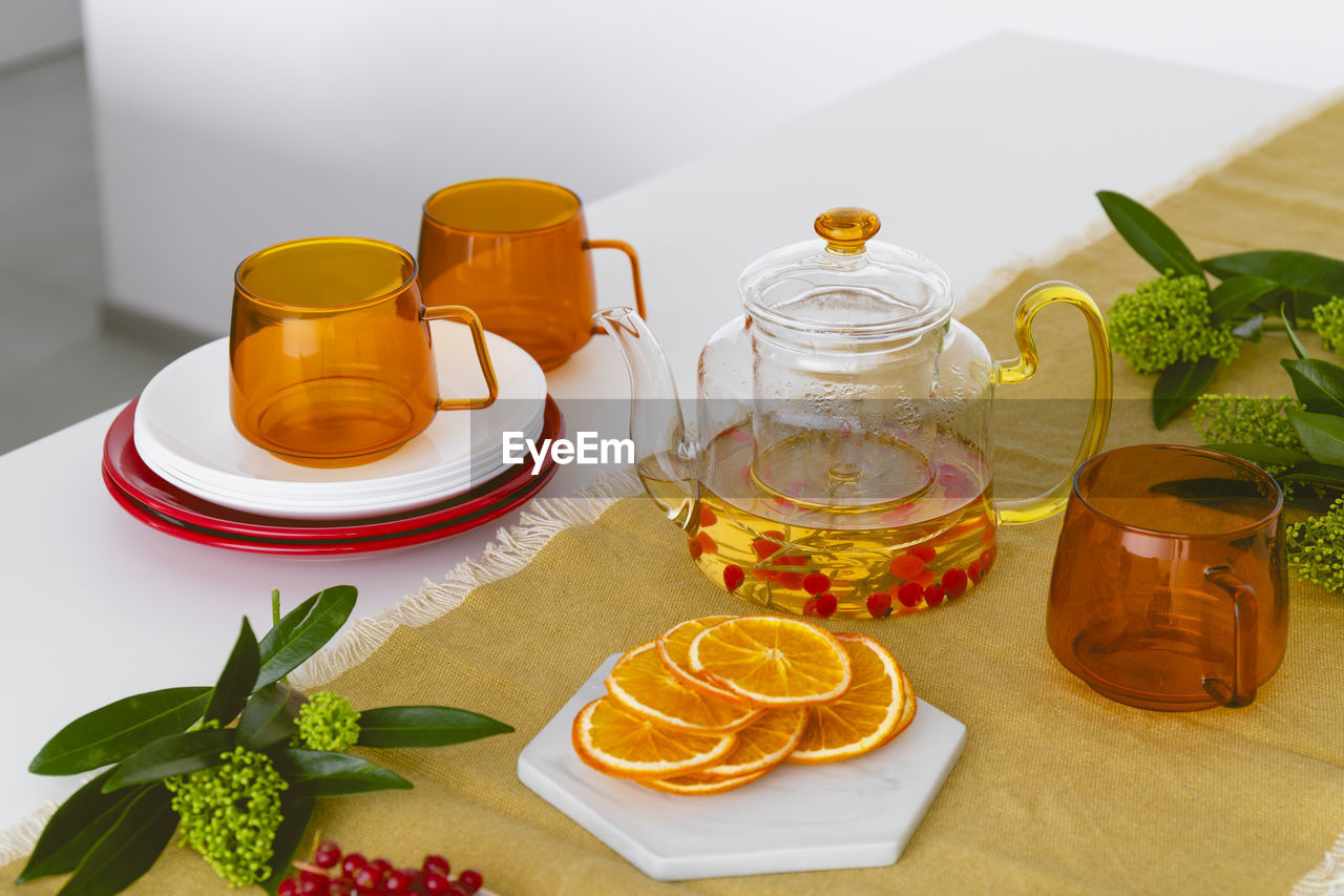 A table setting with orange glass cups, a teapot with tea, fruits and berries.