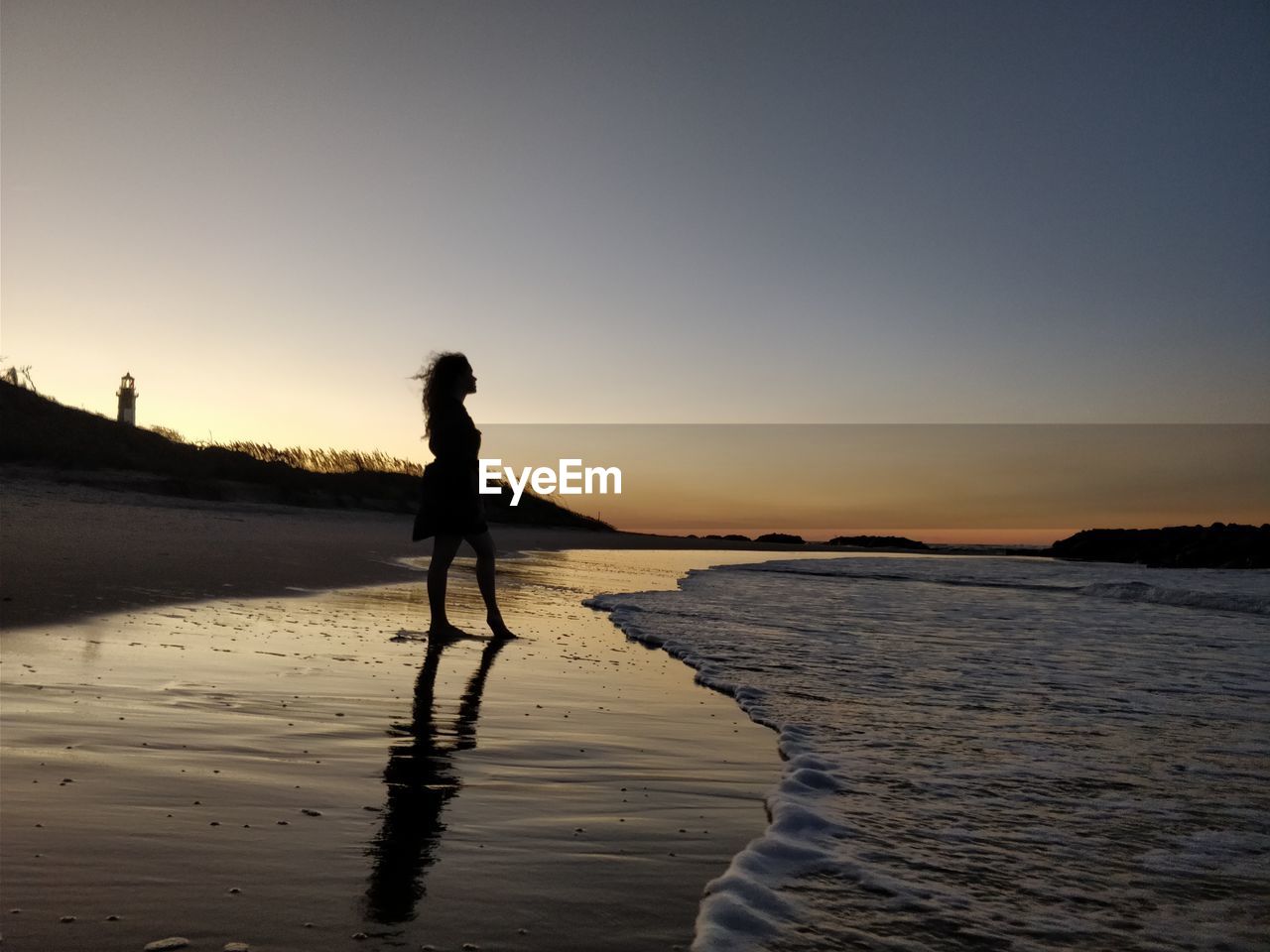 Silhouette young woman standing at beach against clear sky