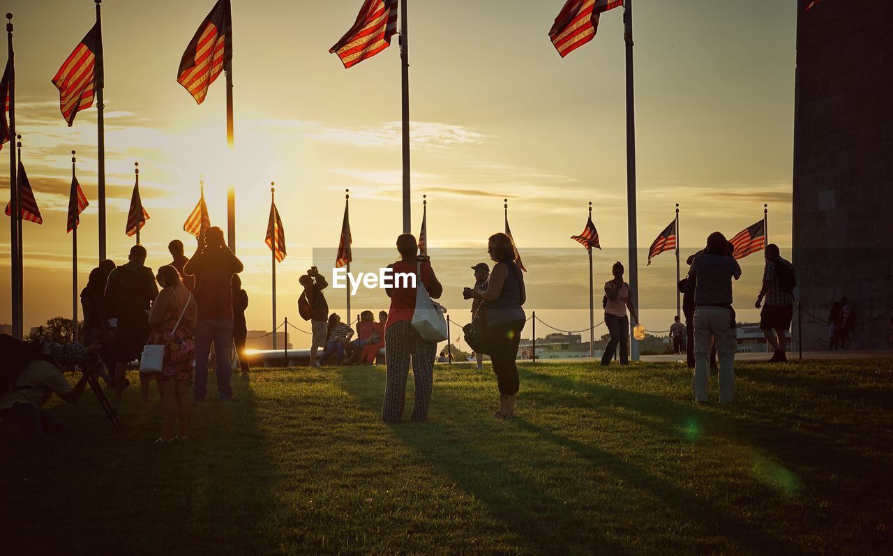 People and american flags on field at washington monument during sunset