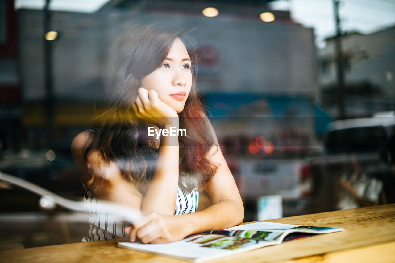 Woman seen through window looking away while sitting in cafe