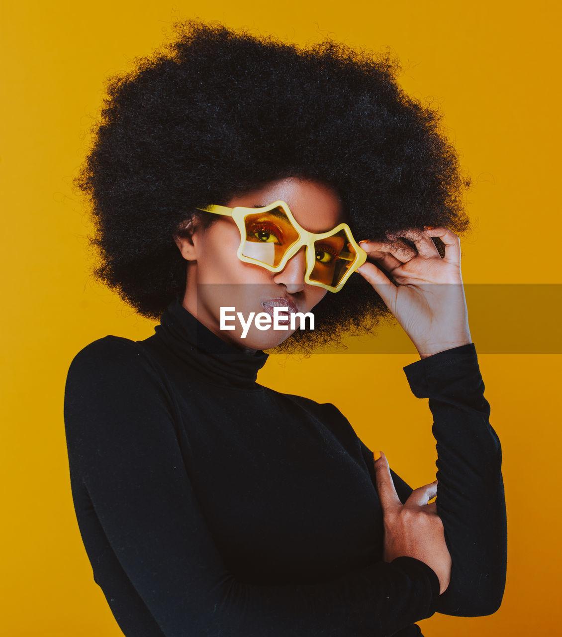 Portrait of young woman wearing sunglasses against yellow background