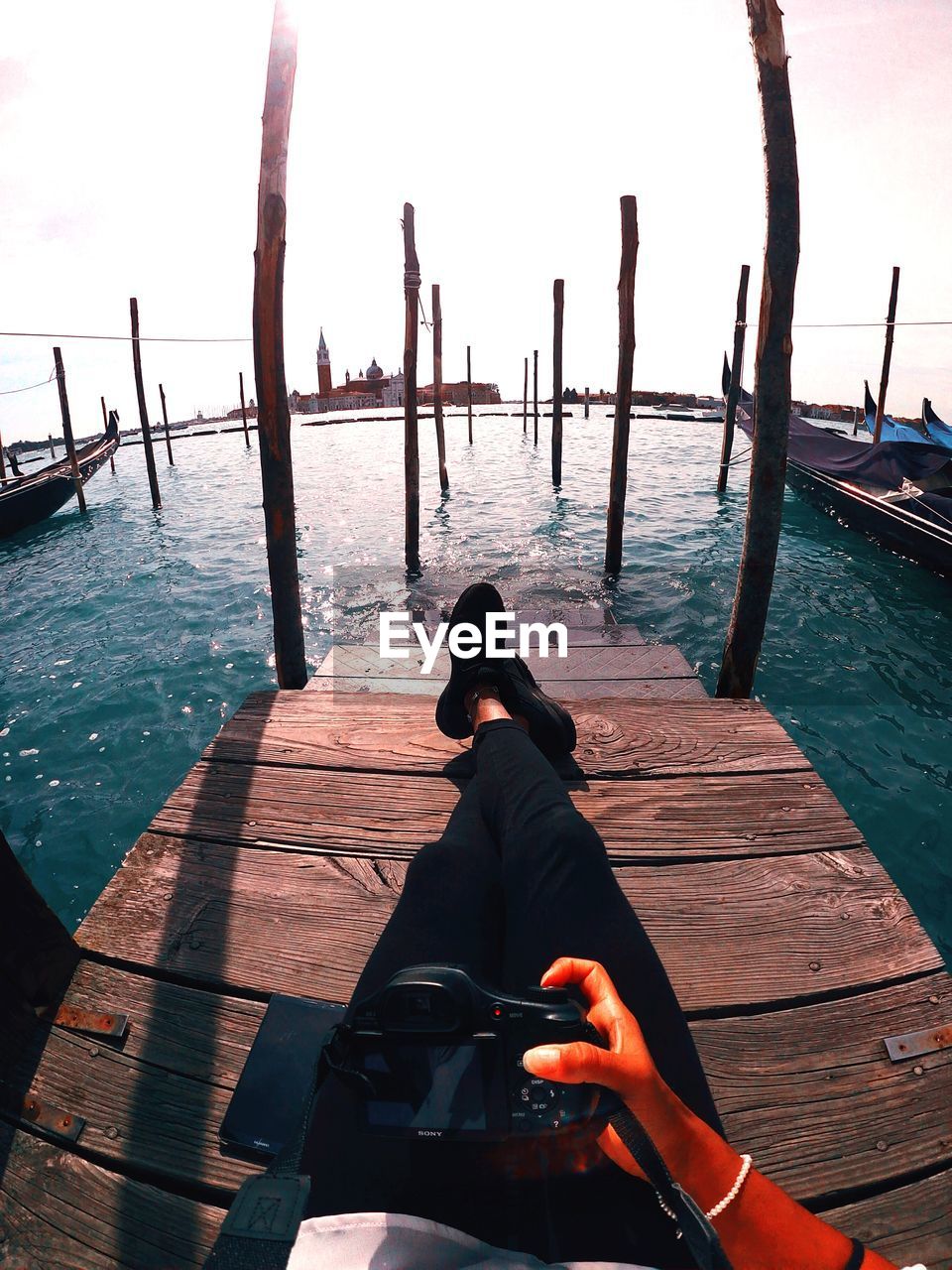 Low section of woman holding camera while sitting on pier