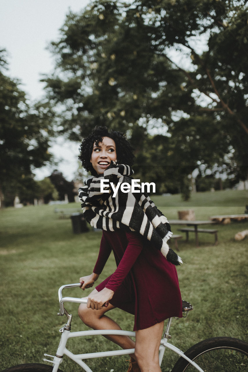 Side view of smiling woman riding bicycle at park