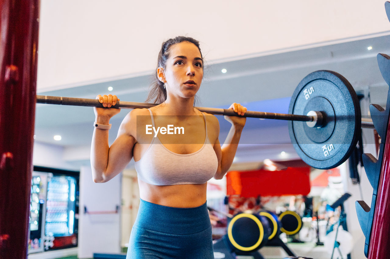 Side view portrait of young woman exercising in gym lifting 