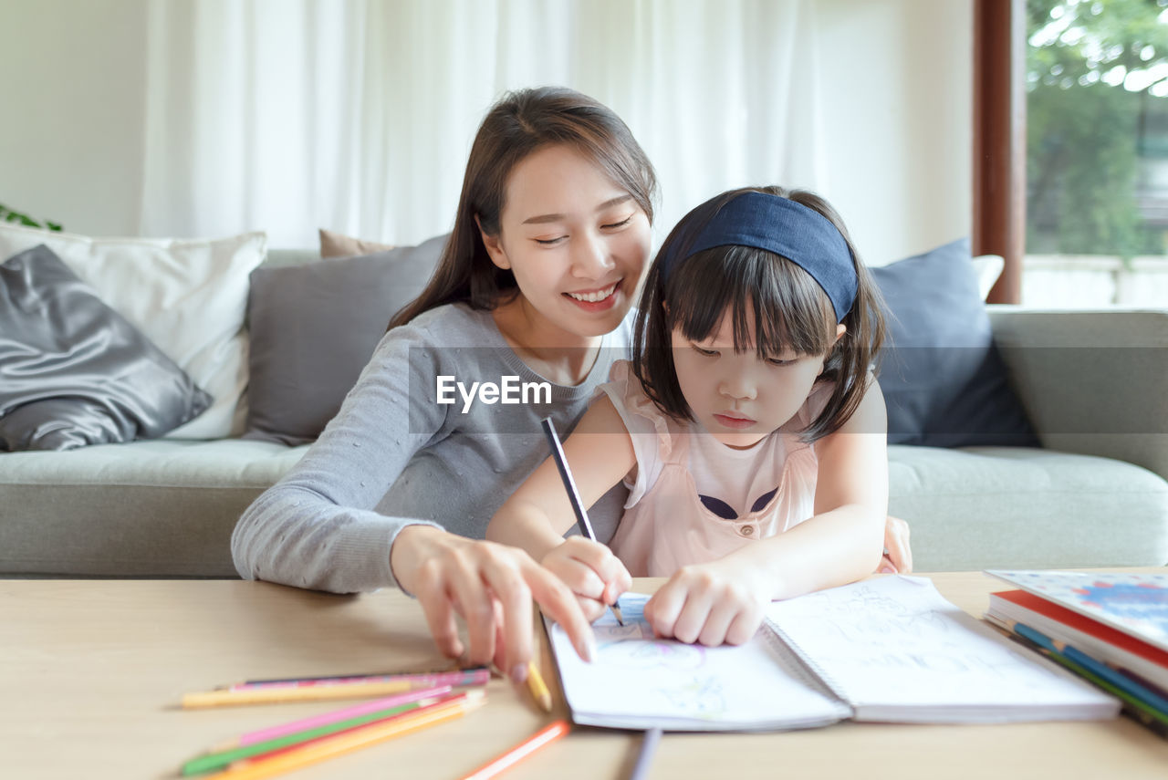 Asian mother teaching her cute kid daughter to studying in living room at home