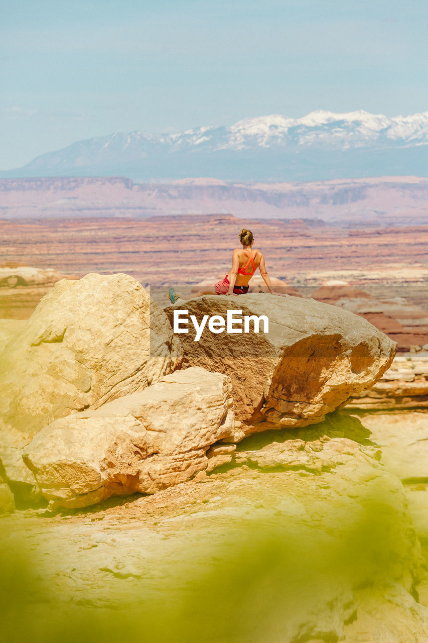 Female hiker in sports bra rests on large rock overlooking canyonlands