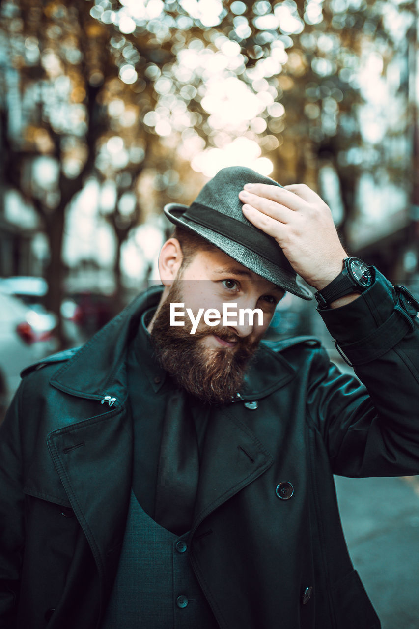 Mid adult man wearing hat looking away while standing against trees