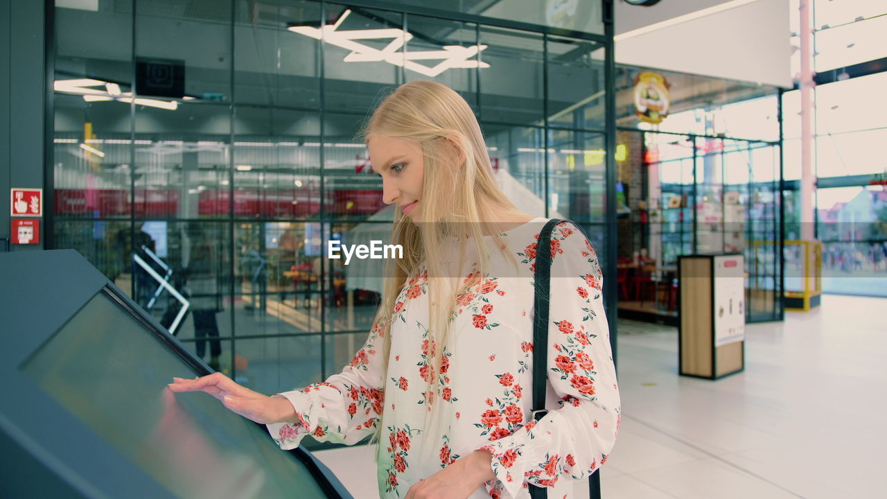 Beautiful woman touching digital screen while standing in shopping mall