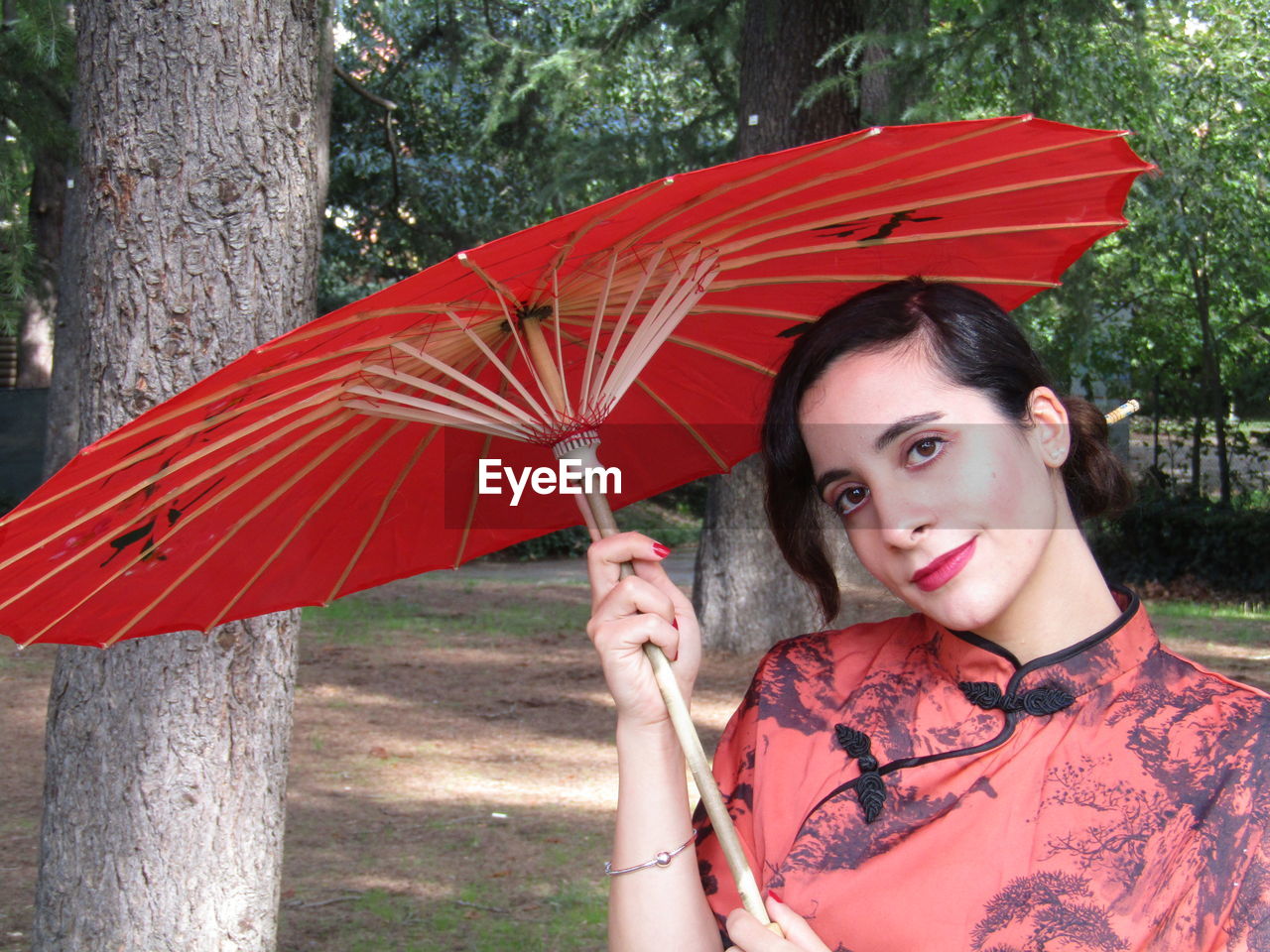 PORTRAIT OF WOMAN WITH UMBRELLA ON TREE TRUNK