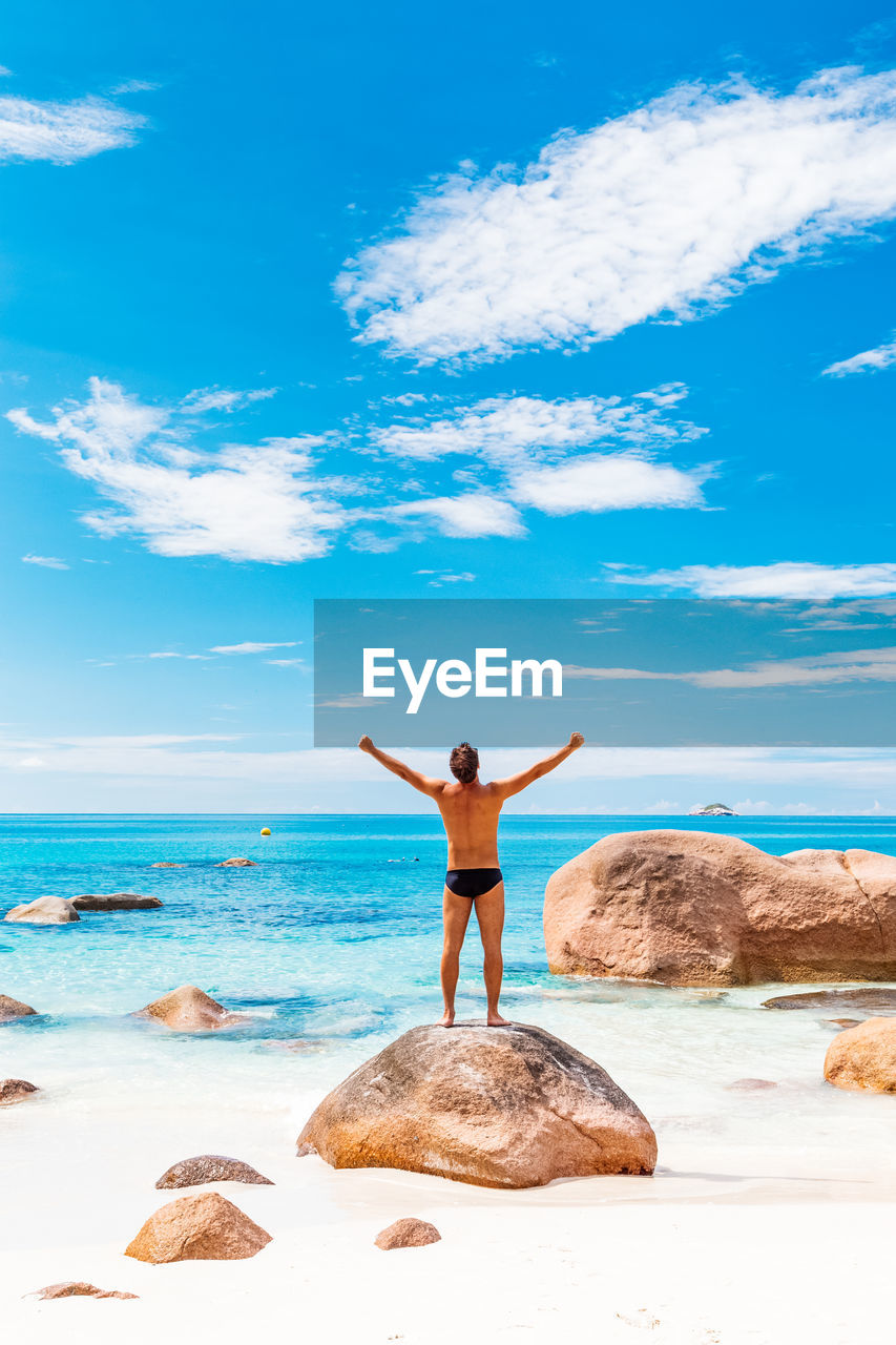 rear view of woman with arms outstretched standing on beach against sky