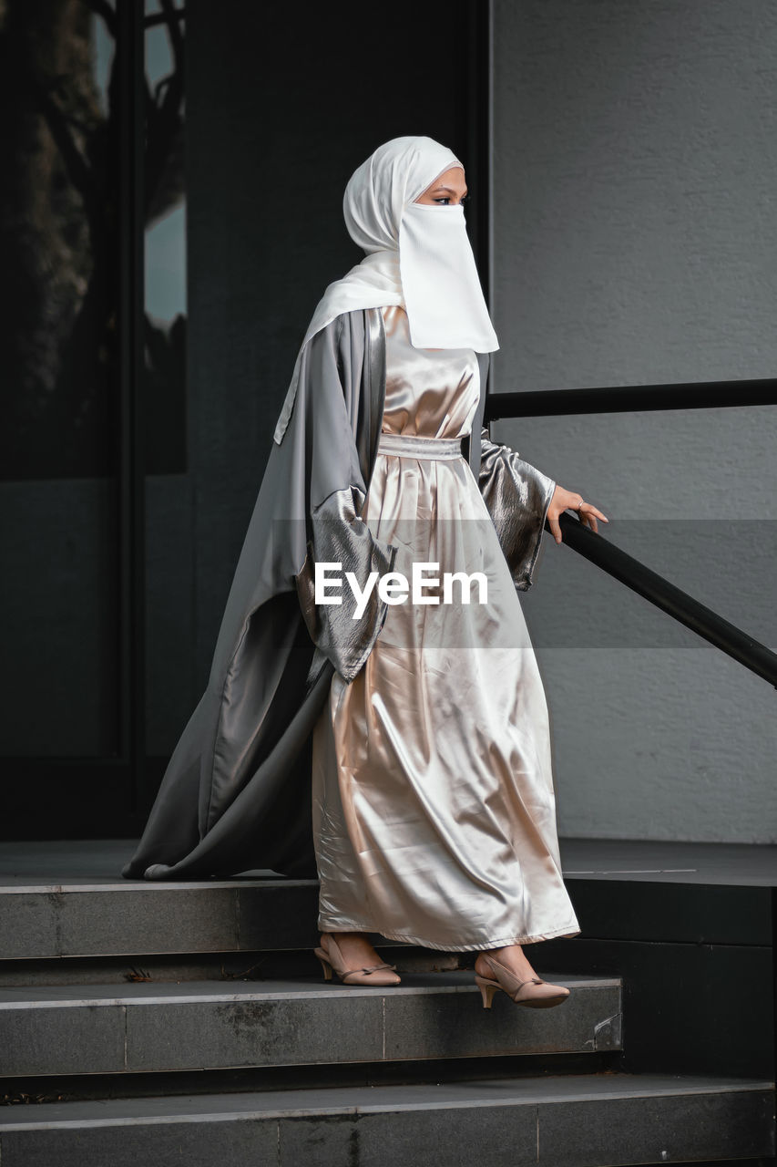 Full length image of veiled woman with white niqab walking down the stairs