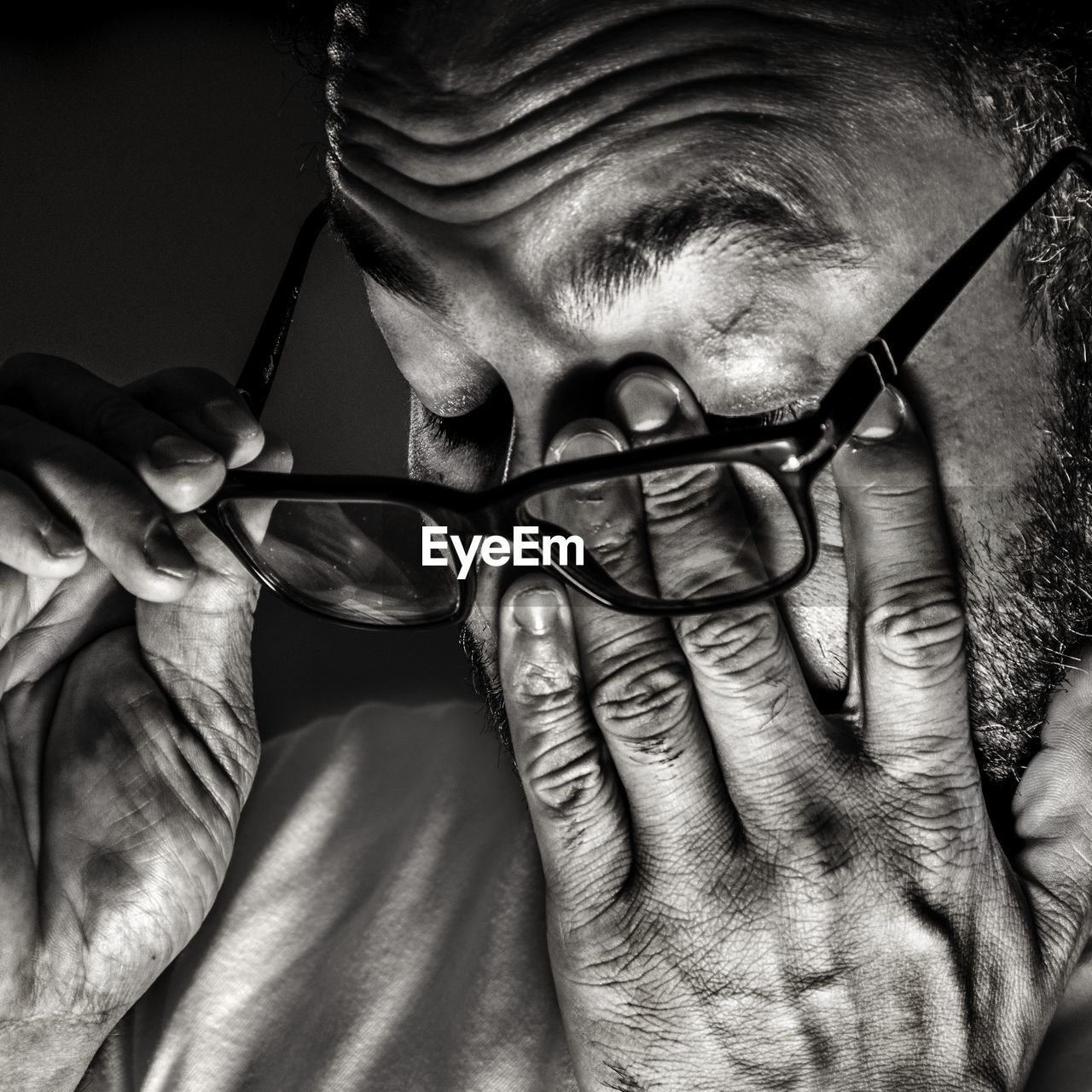 Close-up of man with eyeglasses rubbing eyes against black background