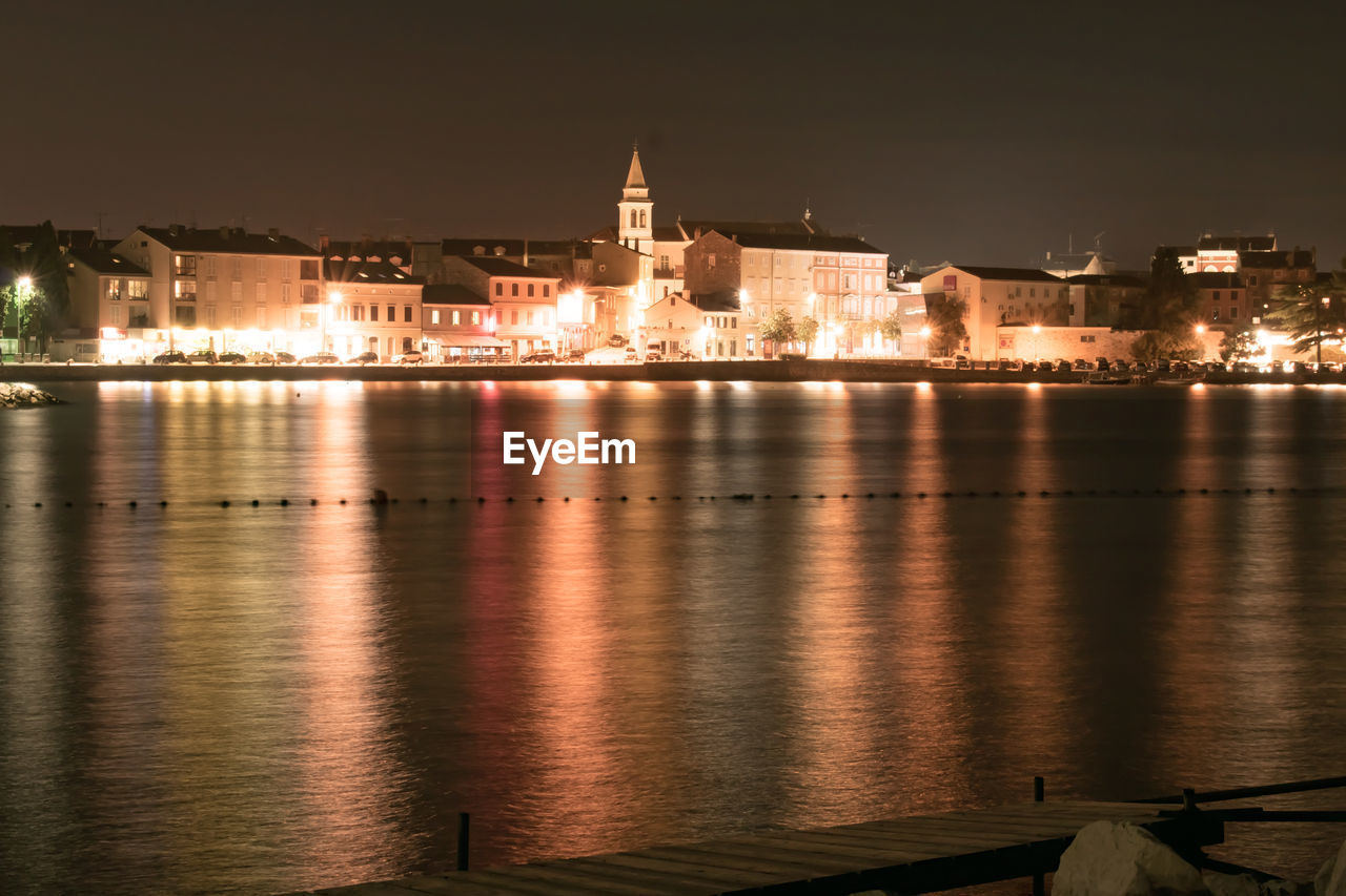 VIEW OF ILLUMINATED BUILDINGS AT WATERFRONT