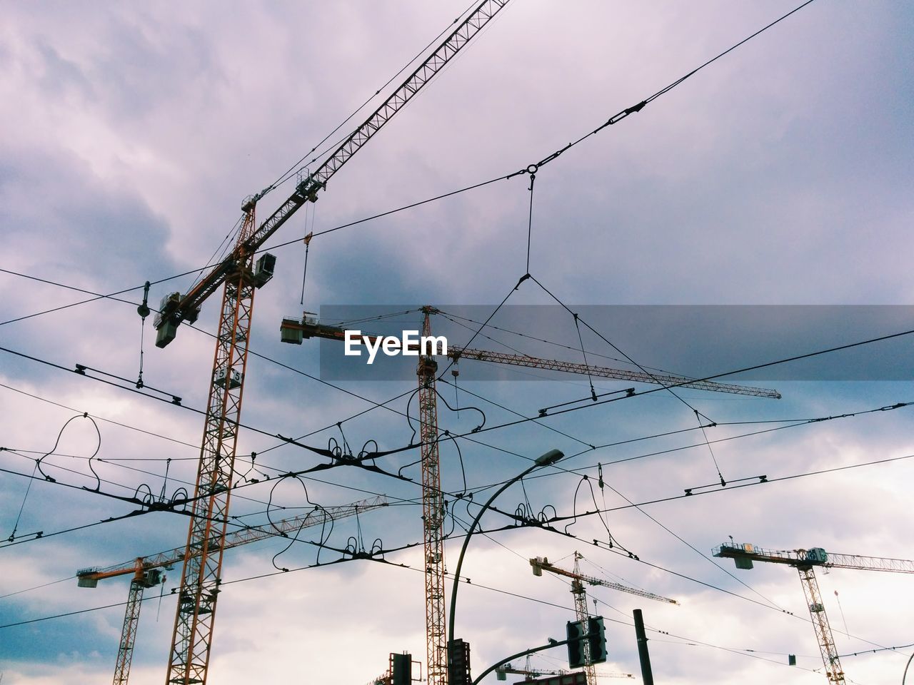 Low angle view of cranes and cables against cloudy sky