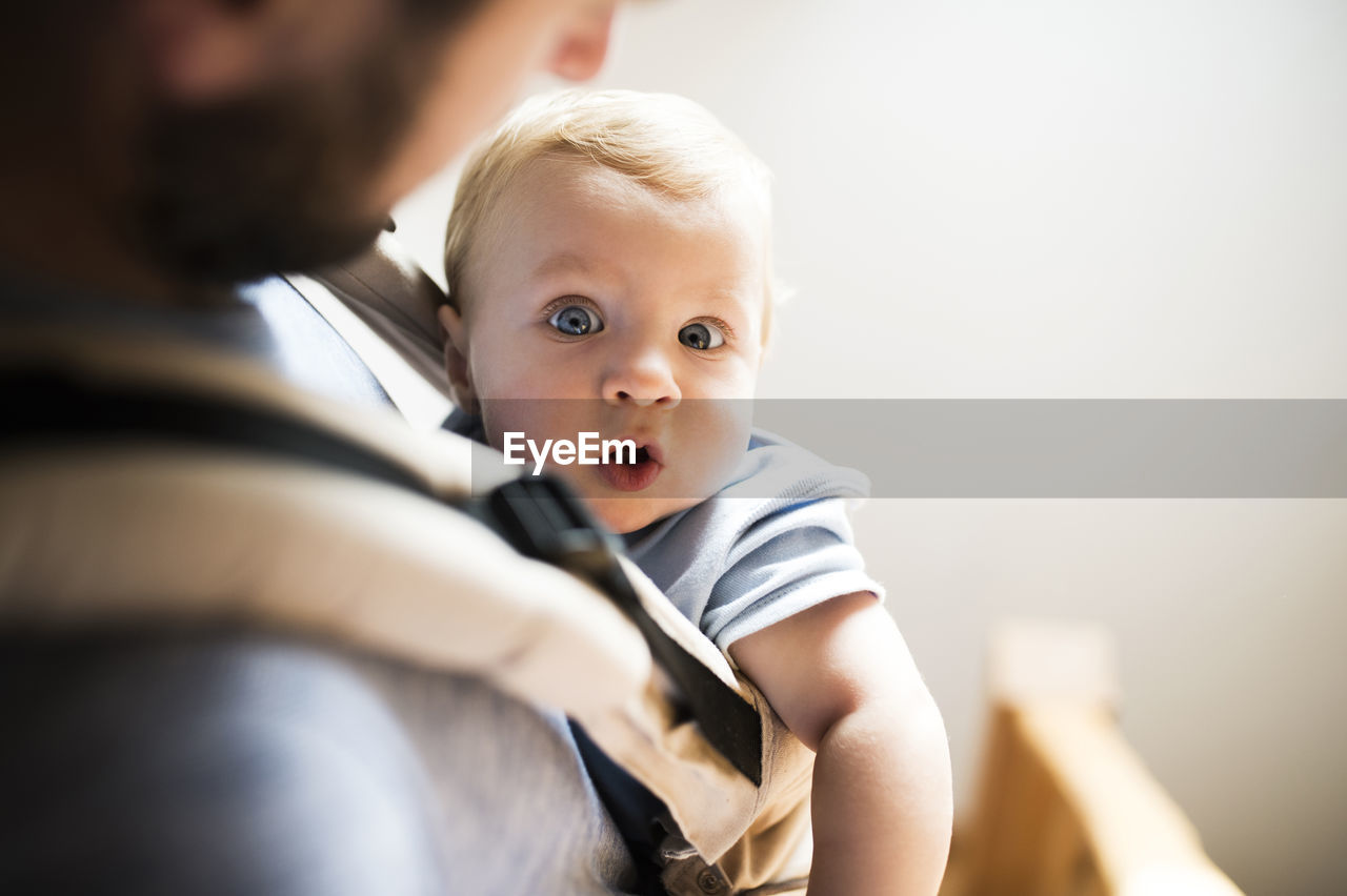 Happy father with baby in baby carrier at home