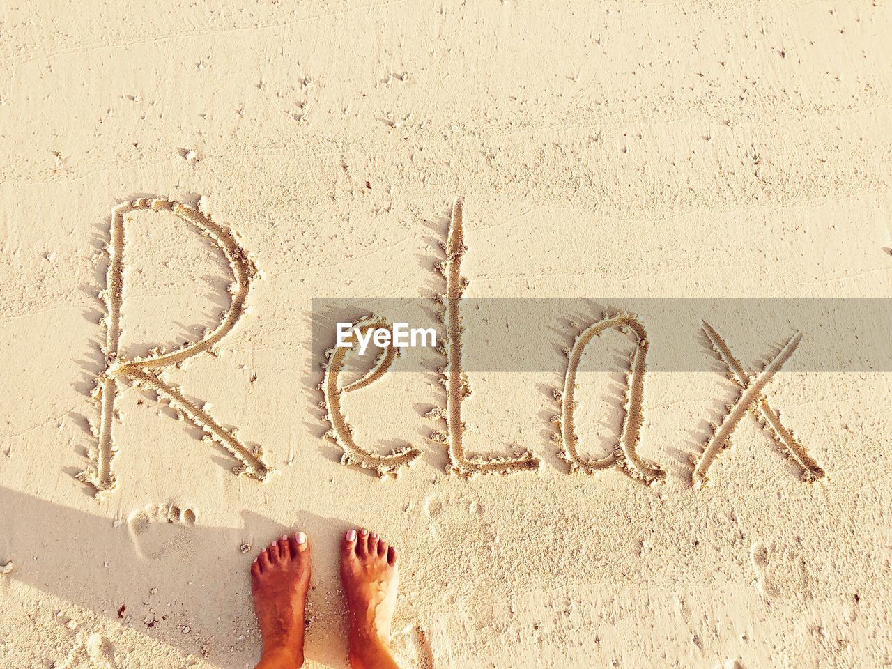 Low section of woman standing by text on sand at beach