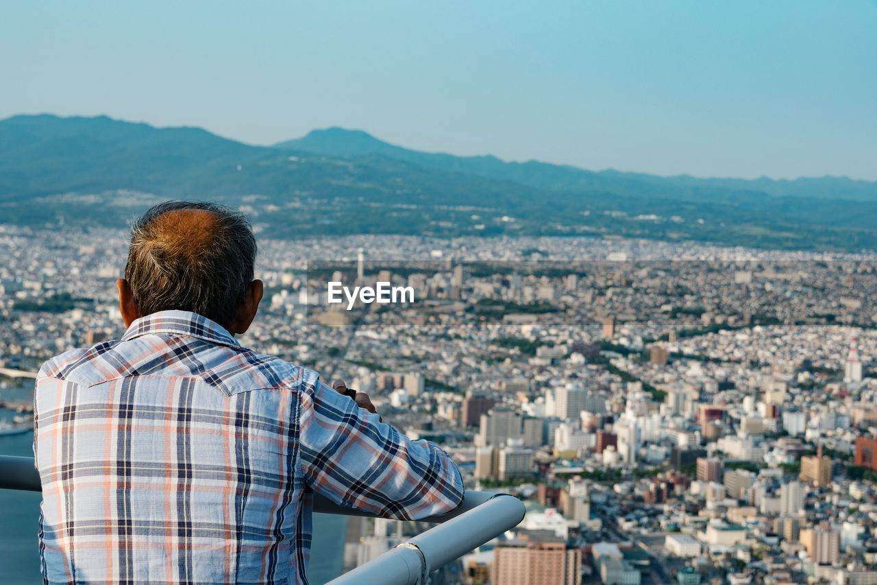 REAR VIEW OF MAN AGAINST CITYSCAPE