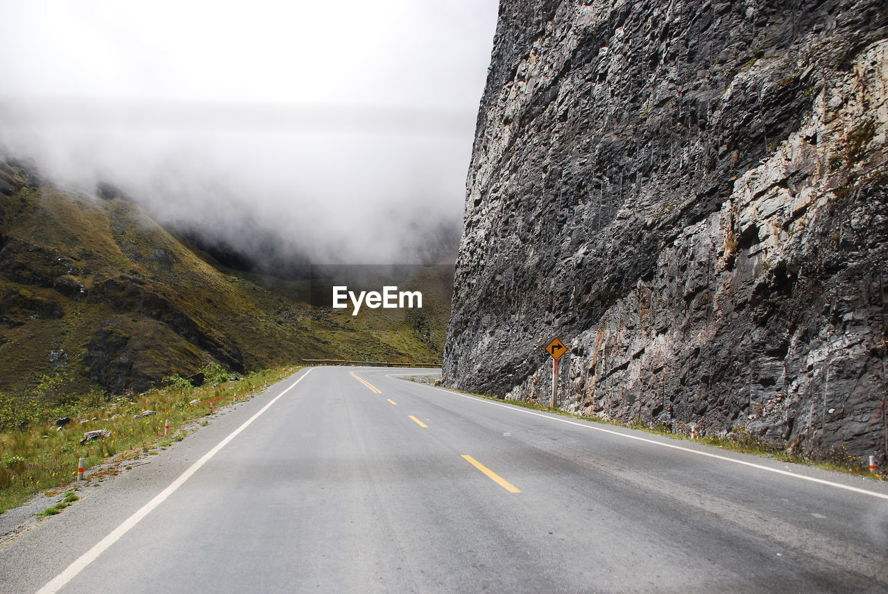 Empty road amidst rocky mountains in foggy weather