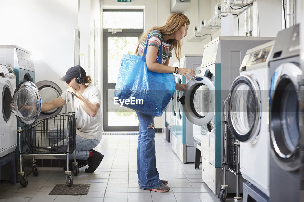 Full length of male and female university students doing laundry at laundromat