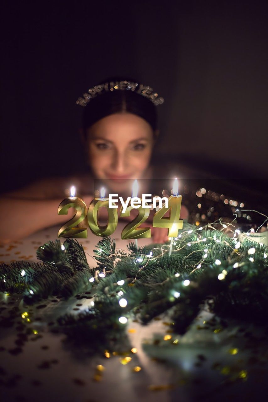 Woman in a gold dress is sitting at a table with candles 2024 in the new year