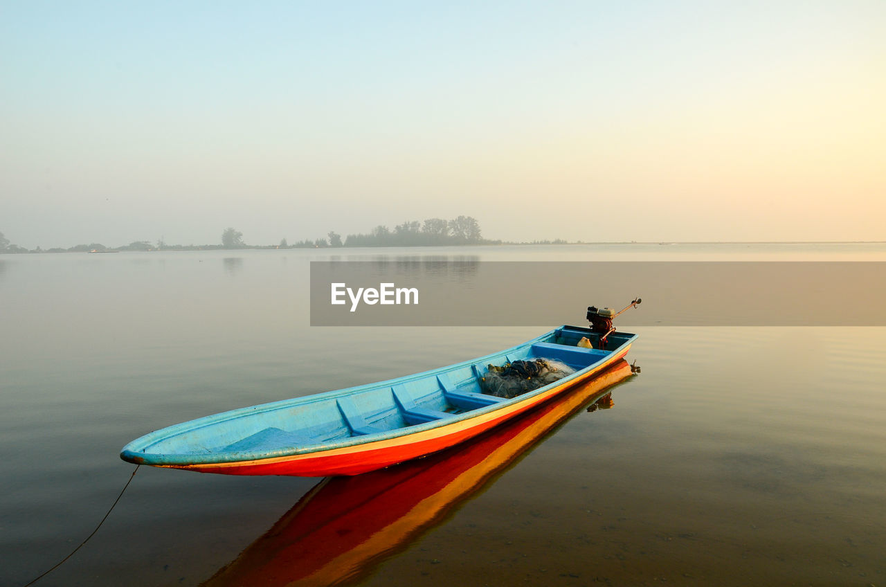 Kayak moored on lake against sky in foggy weather during sunset