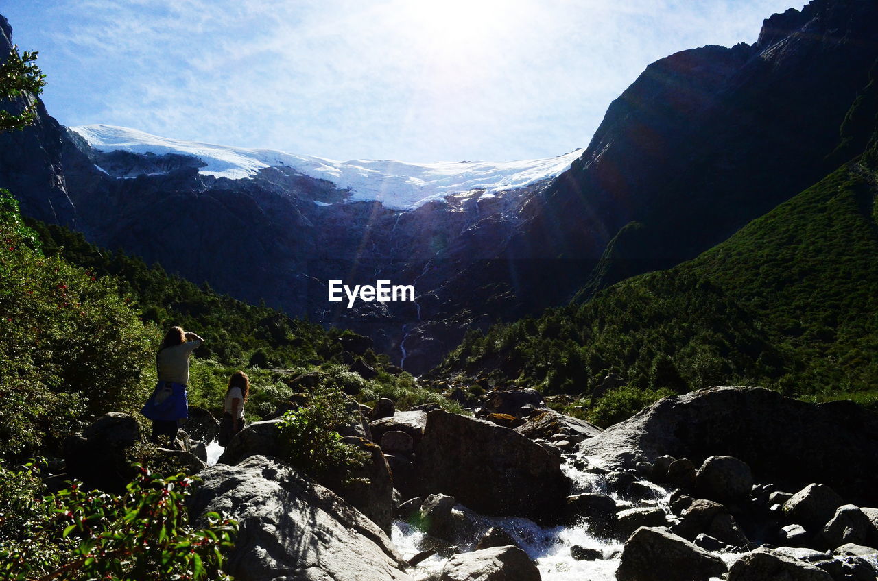 Friends standing on rocks amidst mountain against sky