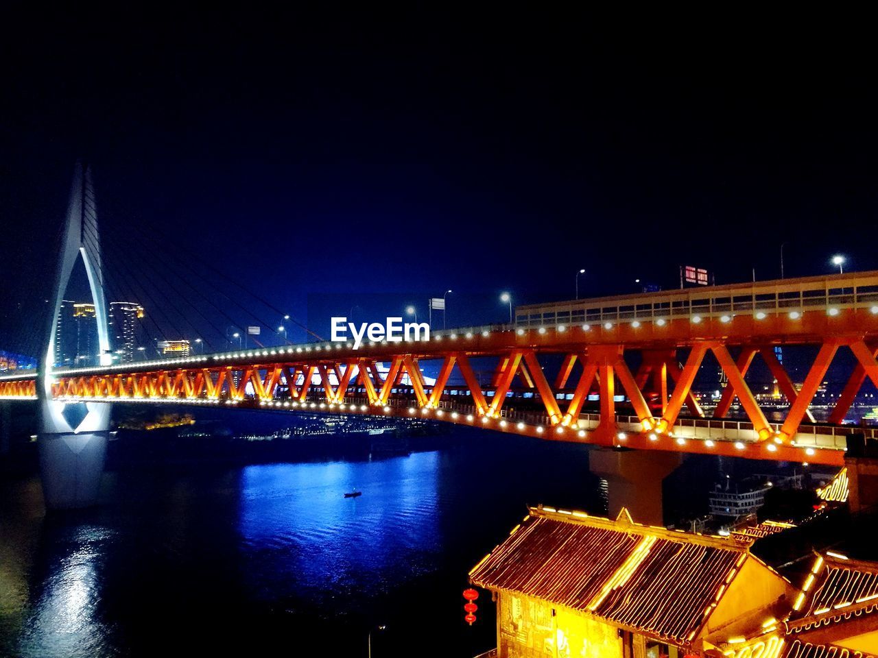 Illuminated bridge over river against sky at night