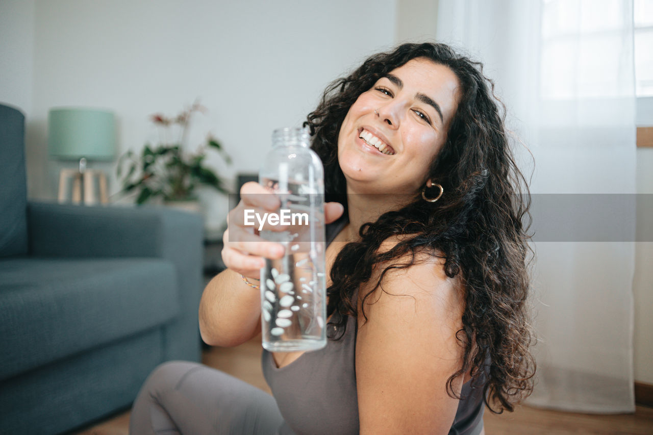 Portrait of young woman holding water bottle at home