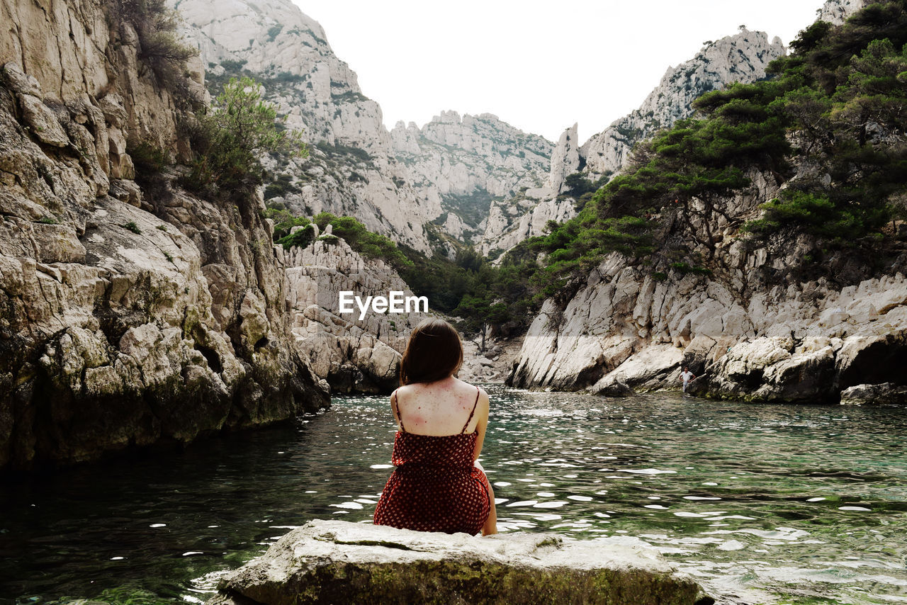 Rear view of woman sitting by lake against rock formations